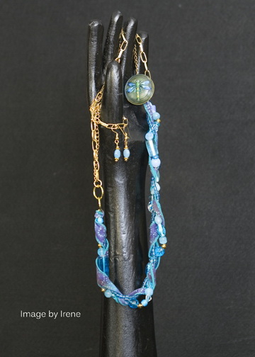 Blue glass beads, silk ribbon, and firefly button on base metal chain, 28” with matching bead earrings on gold plated ear wires.