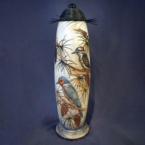 “Woodpecker’s Perch”- Doug turned the vase, Ana Li Gresham wood-burned and painted three types of woodpeckers perched on pine boughs, and Lyn coiled pine needles for the lid, topped by a turned resin knob with an embedded pinecone. 26” x 8”